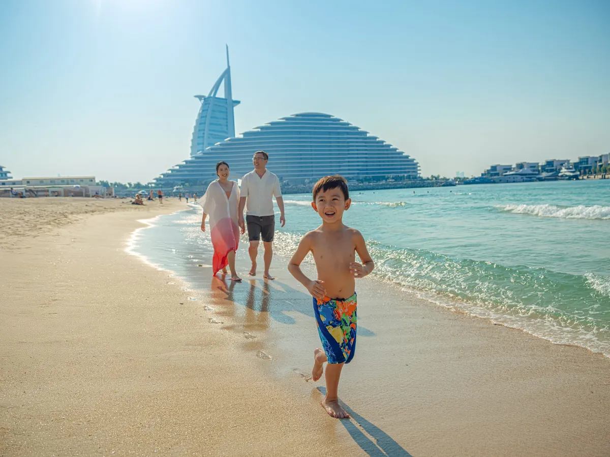 Families and sunbathers enjoying the sandy beach and calm waters at Kite Beach, Dubai.