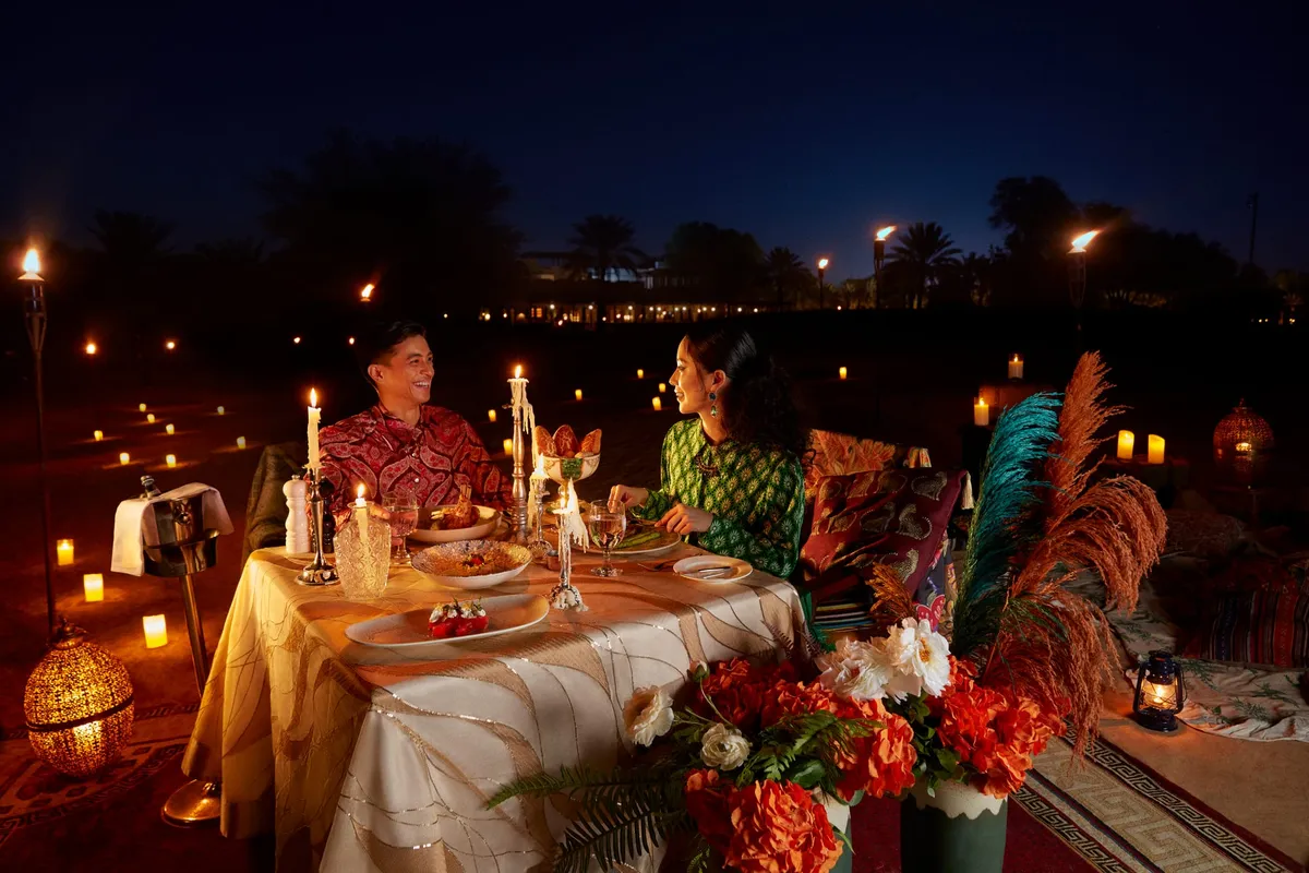 A couple dining at a candlelit outdoor table at Bab Al Shams Desert Resort overlooking a still pool
